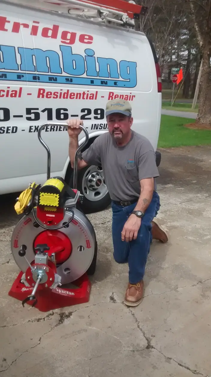 Johnny Eastridge kneeling beside the drum sewer cleaning machine at the back of the Eastridge Plumbing van