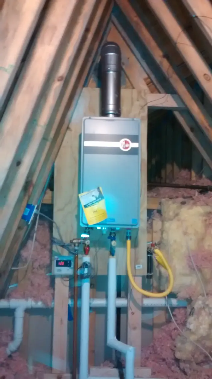 A tankless water heater mounted in an attic, with its gas supply line and vent piping connected
